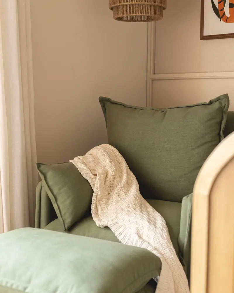 Sillón tapizado en verde con almohadones y una manta tejida